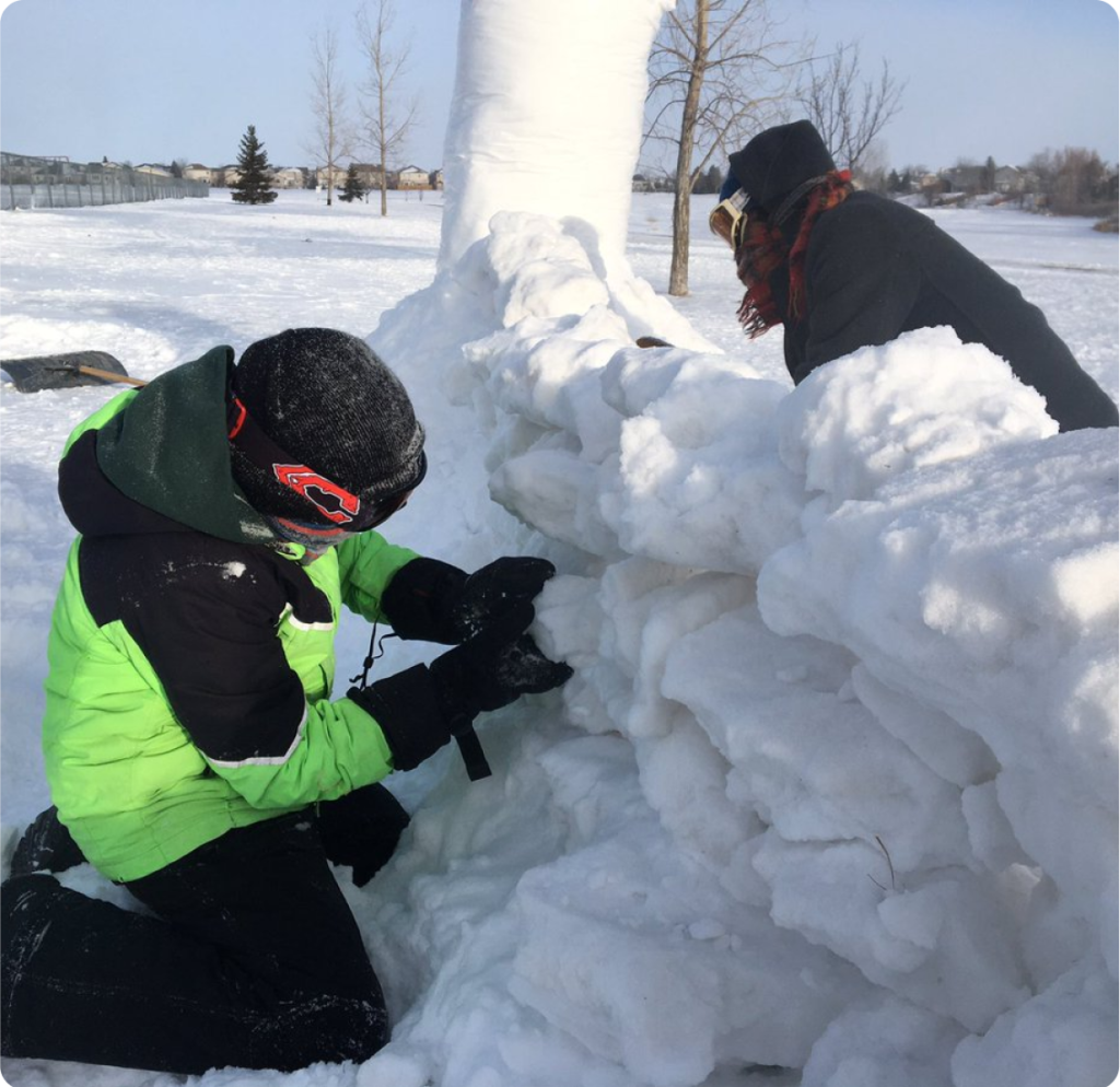 Two people building a wall out of chunks of snow.